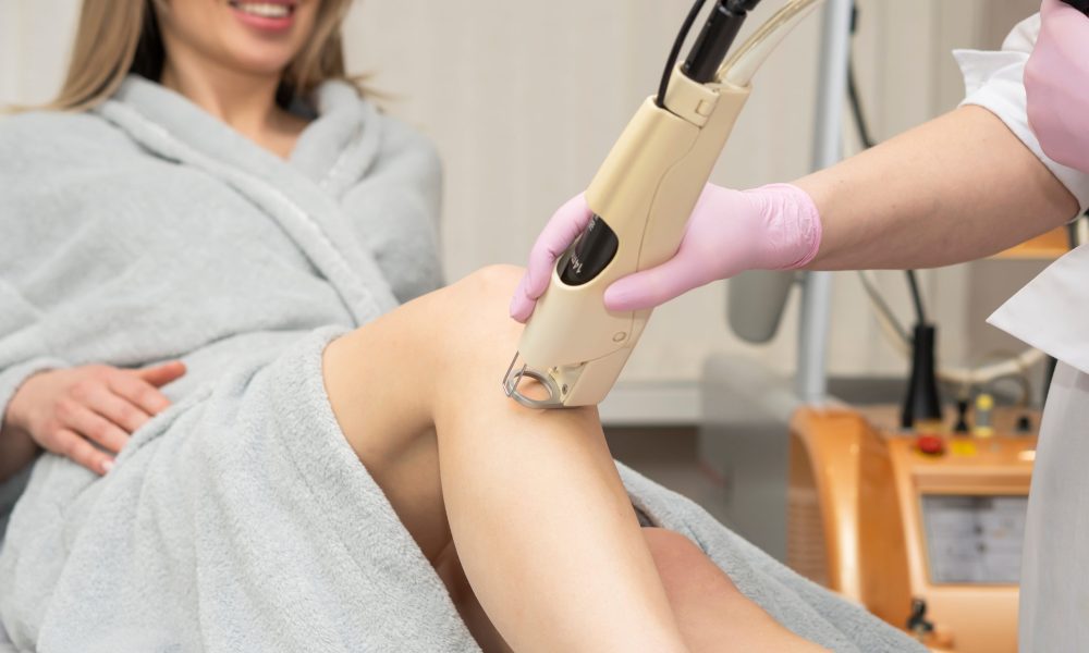 Bare HR Laser Hair Removal | Cosmetologist holds the maniple of the laser hair removal device along the slender beautiful legs of a woman, removing hair. laser hair and tattoo removal. laser rejuvenation | Sculpted Aesthetics in Columbia, SC