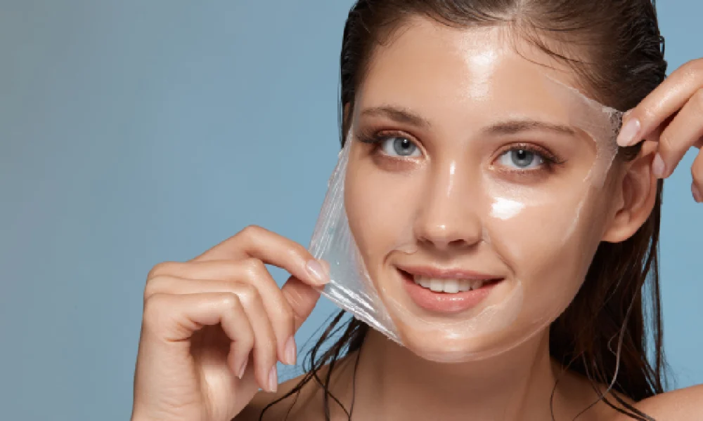 Smiling young woman peeling off a clear facial mask, revealing smooth and glowing skin, symbolizing the rejuvenating effects of chemical peels in Columbia, SC